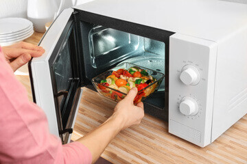 Personne plaçant un plat cuisiné dans un micro-ondes