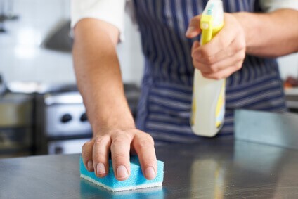 Personnel de cuisine nettoyant un plan de travail en inox pour limiter la propagation des mouches