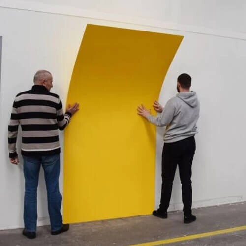 Deux personnes en train de poser une plaque de PVC jaune comme revêtement mural dans une cuisine professionnelle