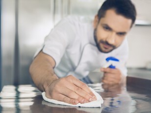 Personnel de cuisine nettoyant un plan de travail en inox pour limiter la propagation des mouches
